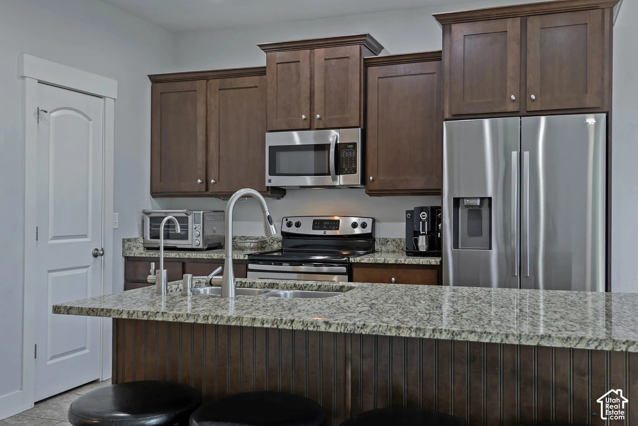 Kitchen featuring rich wood cabinetry, stainless steel appliances, granite countertops, and a kitchen island with beadboard paneling