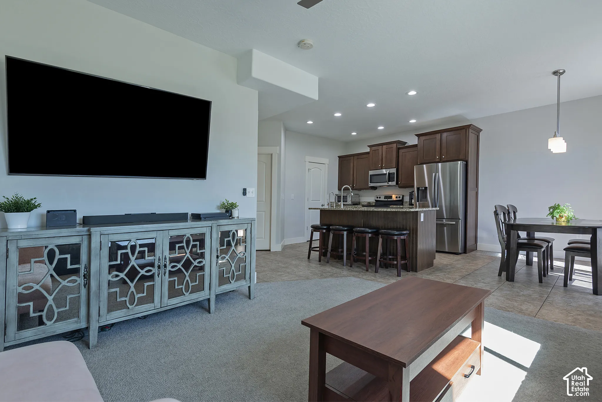 Open concept living area with carpet flooring, leading to a kitchen featuring wood cabinetry, stainless steel appliances, and a central island with bar seating