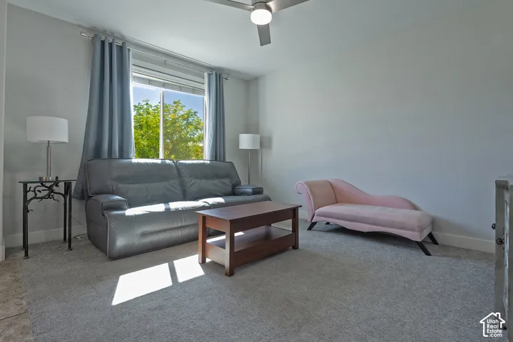 Expansive room featuring light gray walls, a window with a neutral frame, a ceiling fan with integrated lighting, and neutral carpet flooring