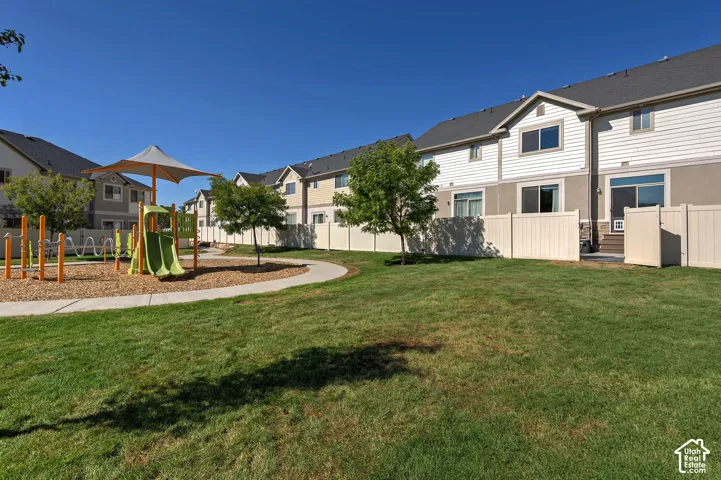 Expansive green space featuring a playground with a shade structure, a winding paved path, and mature trees