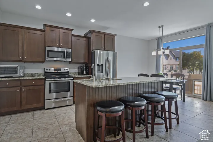 Kitchen featuring wood cabinetry, stainless steel appliances, granite countertops, a center island with bar seating, and tile flooring