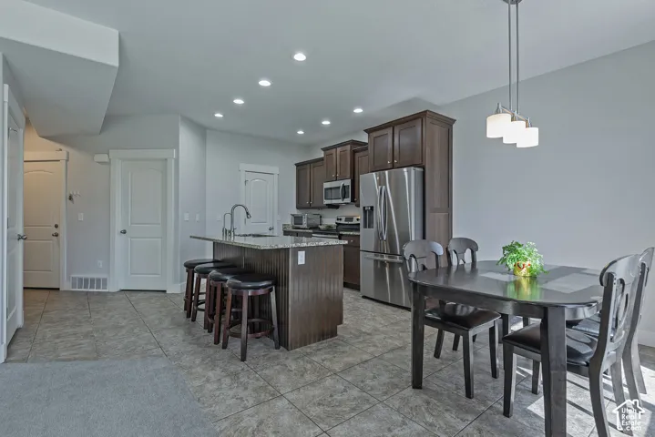Kitchen with dark wood cabinetry, stainless steel appliances, recessed lighting, and a center island with a built-in sink