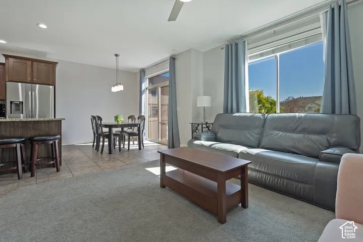 Open-concept living area with carpet and tile flooring, a kitchen island with built-in cabinetry, stainless steel appliances, and a glass sliding door