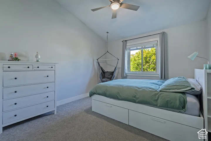 Sloped ceiling room featuring a ceiling fan with light fixture, carpeted flooring, and a window with white trim