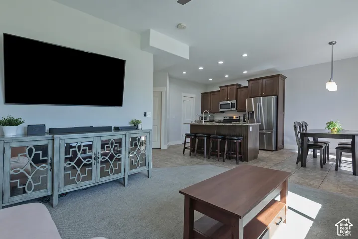 Open concept living area with carpet flooring, leading to a kitchen featuring wood cabinetry, stainless steel appliances, and a central island with bar seating
