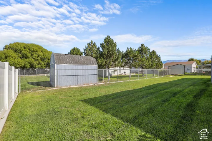Expansive backyard featuring a manicured lawn, chain-link fencing, and a storage shed with a gambrel roof