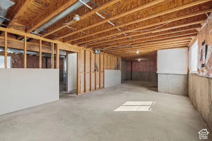 Unfinished lower level featuring exposed wood joists, concrete flooring, and framing for future development
