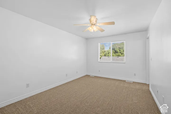 Neutral wall paint, carpet flooring, a ceiling fan with integrated lighting, and a window providing natural light
