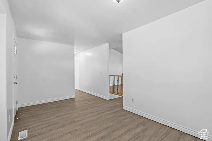 Wood-finish flooring, white painted walls, and a staircase with wood railing and black balusters