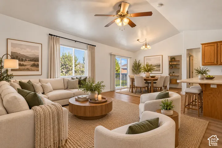 Vaulted ceilings featuring a central paddle fan, wood-finish flooring, sliding glass door, kitchen breakfast bar, and built-in shelving