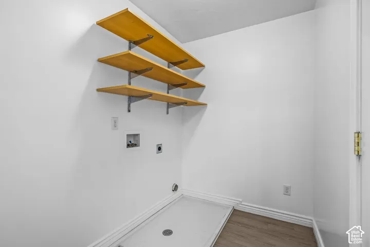 Laundry area featuring three wood shelves, white walls, and wood-finish flooring