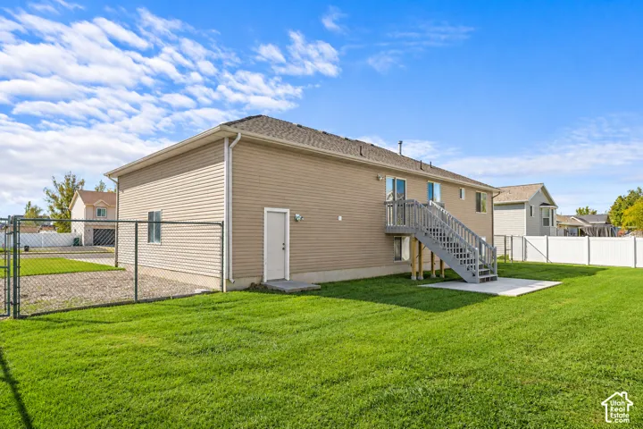 Rear exterior featuring vinyl siding, an elevated wood deck with stairs, a ground-level concrete patio, and a fully fenced yard