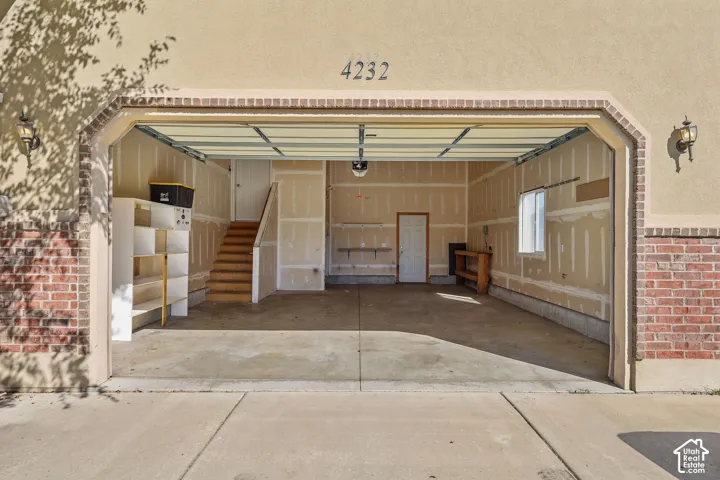 Attached garage with a concrete floor, interior staircase, and wall-mounted shelving