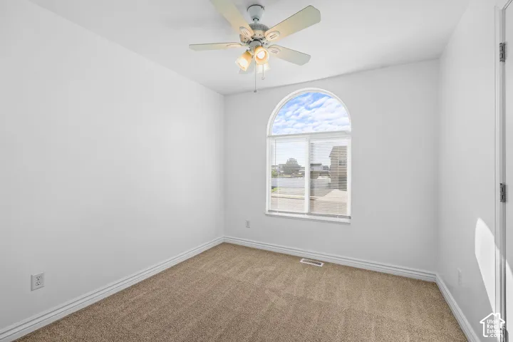 Arched window, ceiling fan with light fixture, neutral carpeting, and white walls