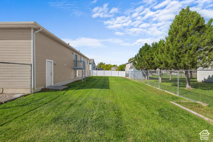 Expansive green lawn, chain link fencing, mature evergreen trees, light-colored siding, and a second-story balcony