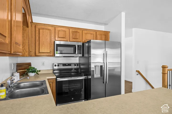 Kitchen featuring wood cabinetry, stainless steel appliances, a double basin sink, and laminate countertops