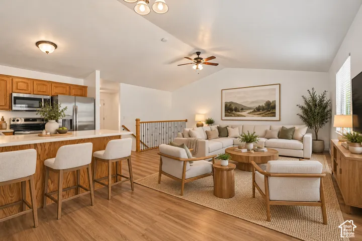 Open-concept interior featuring vaulted ceilings, wood-finish flooring, a kitchen island with stone countertop, stainless steel appliances, and a metal-spindle staircase railing