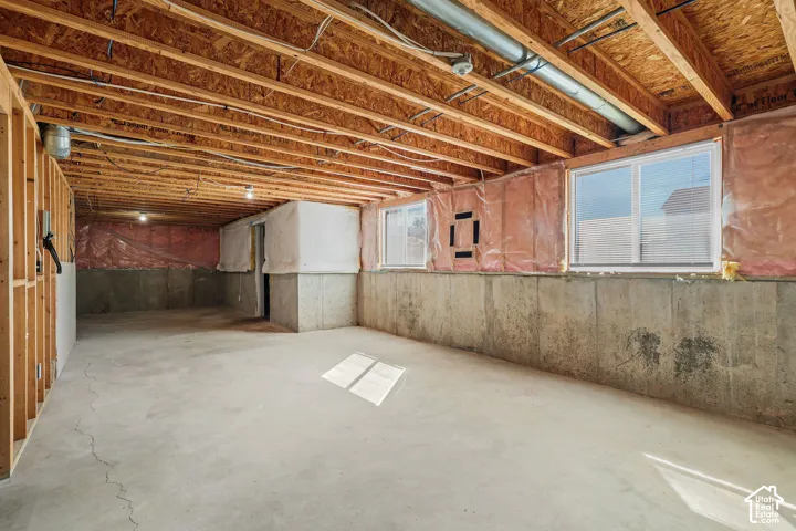 Unfinished concrete basement with exposed wood joists and subfloor, featuring two windows and framed walls