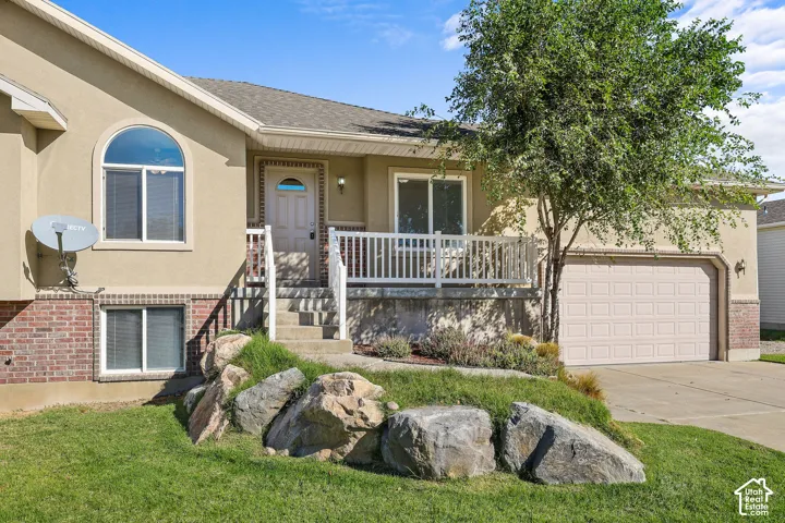 Stucco exterior with brick detailing, arched and rectangular windows, a front porch with white railing, a two-car garage, and established landscaping