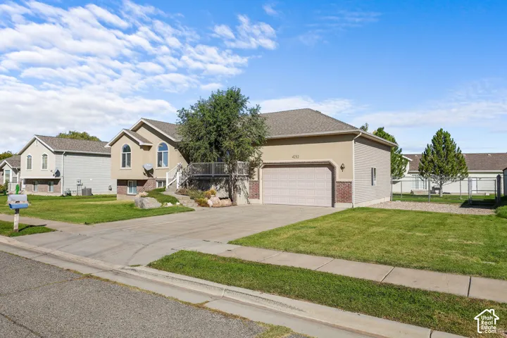 Stucco exterior with brick detailing, attached garage, concrete driveway, and a front yard with mature landscaping