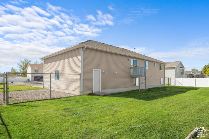 Spacious backyard featuring a chain-link fence, a white privacy fence, a second-story balcony, and a side-entry door