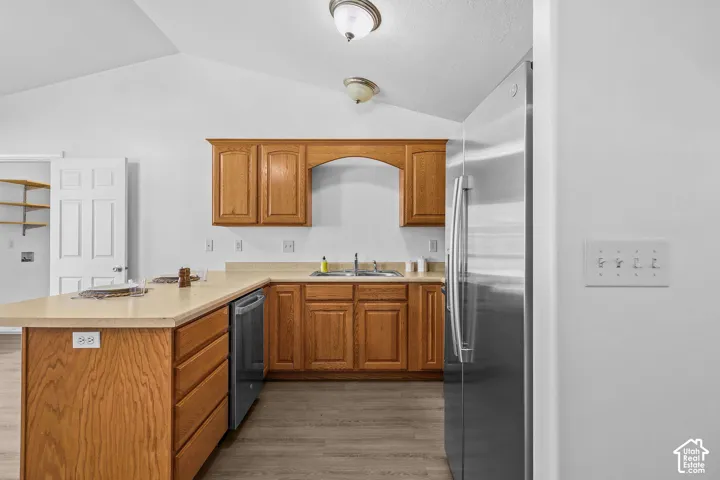 Kitchen featuring wood cabinetry, light-toned countertops, a stainless steel refrigerator, and a stainless steel dishwasher