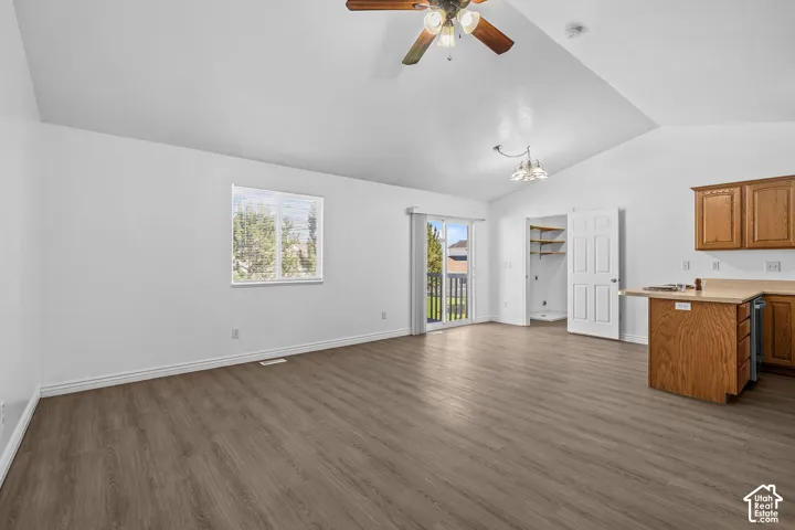 Vaulted ceilings, wood-finish flooring, sliding glass door with balcony access, warm wood cabinetry, and a ceiling fan