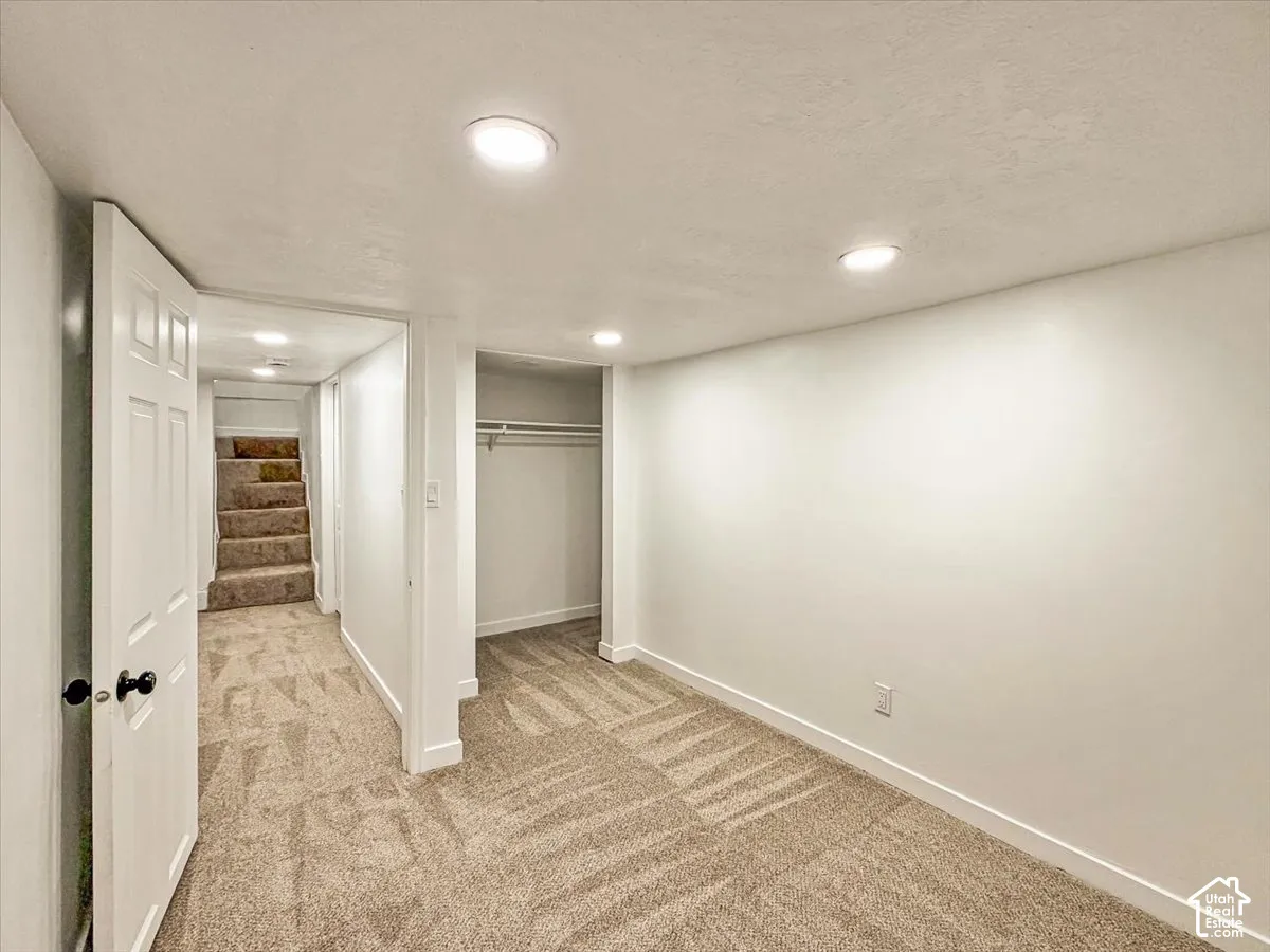 Recessed ceiling lighting, neutral-toned carpet, white painted walls, and an open closet space