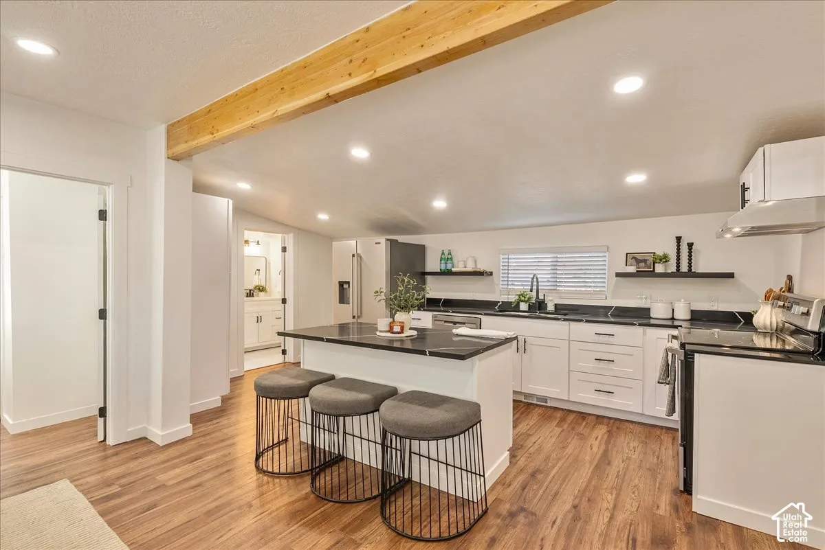 Kitchen featuring wood-finish flooring, white cabinetry, black countertops, and a central island