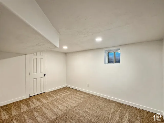 Recessed lighting, wall-to-wall carpeting with geometric pattern, white paneled door with dark hardware, and a single window
