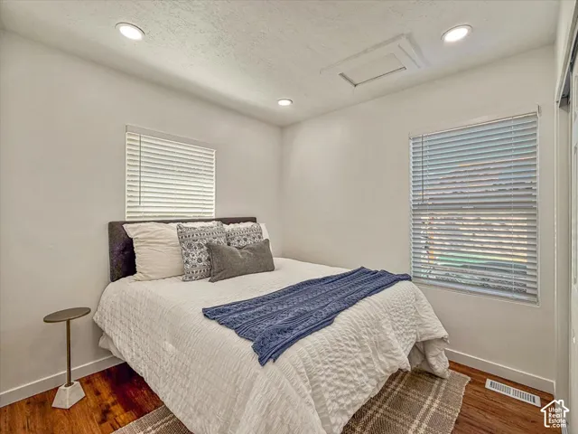 Recessed ceiling lighting, two windows with blinds, wood-finish flooring, and white wall finishes