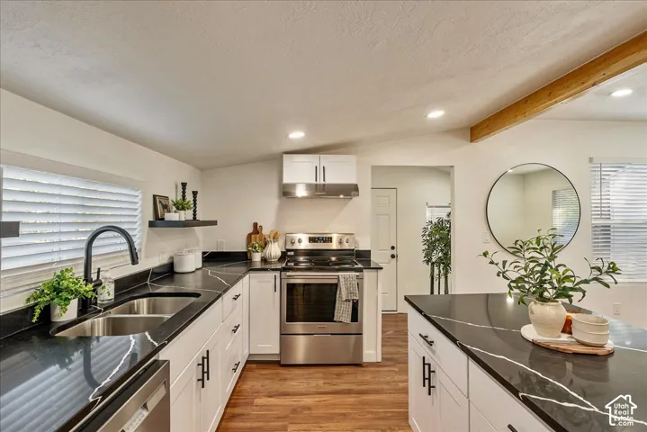Kitchen featuring white cabinetry, dark countertops with light veining, wood-finish flooring, a stainless steel range, and a dual basin sink with a matte black faucet