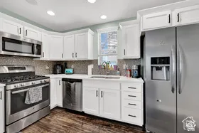 Kitchen featuring white cabinetry, stainless steel appliances, mosaic tile backsplash, wood-finish flooring, and recessed lighting