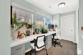 Built-in desk with a white countertop, multiple windows with blinds, light blue wall paint, a white paneled door, and a flush mount ceiling light