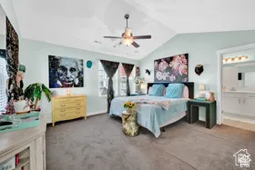 Vaulted ceiling with ceiling fan, light-toned wall paint, gray carpet flooring, window with blinds, and an attached bathroom featuring a double vanity with two sinks and a multi-bulb light fixture