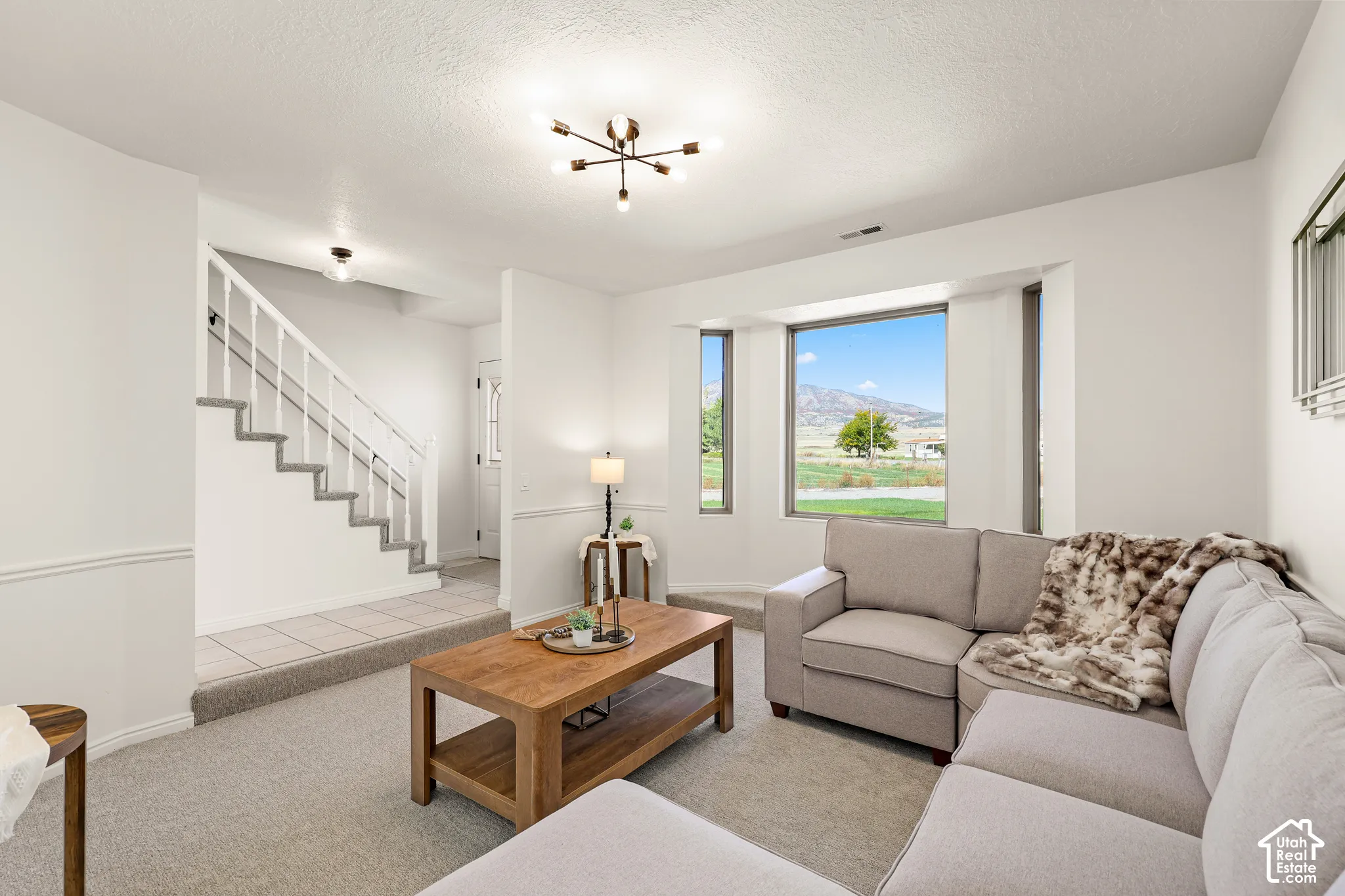 Bay window with mountain scenery, staircase with carpeted treads, tile flooring entryway, carpeted living area, and a modern ceiling light fixture