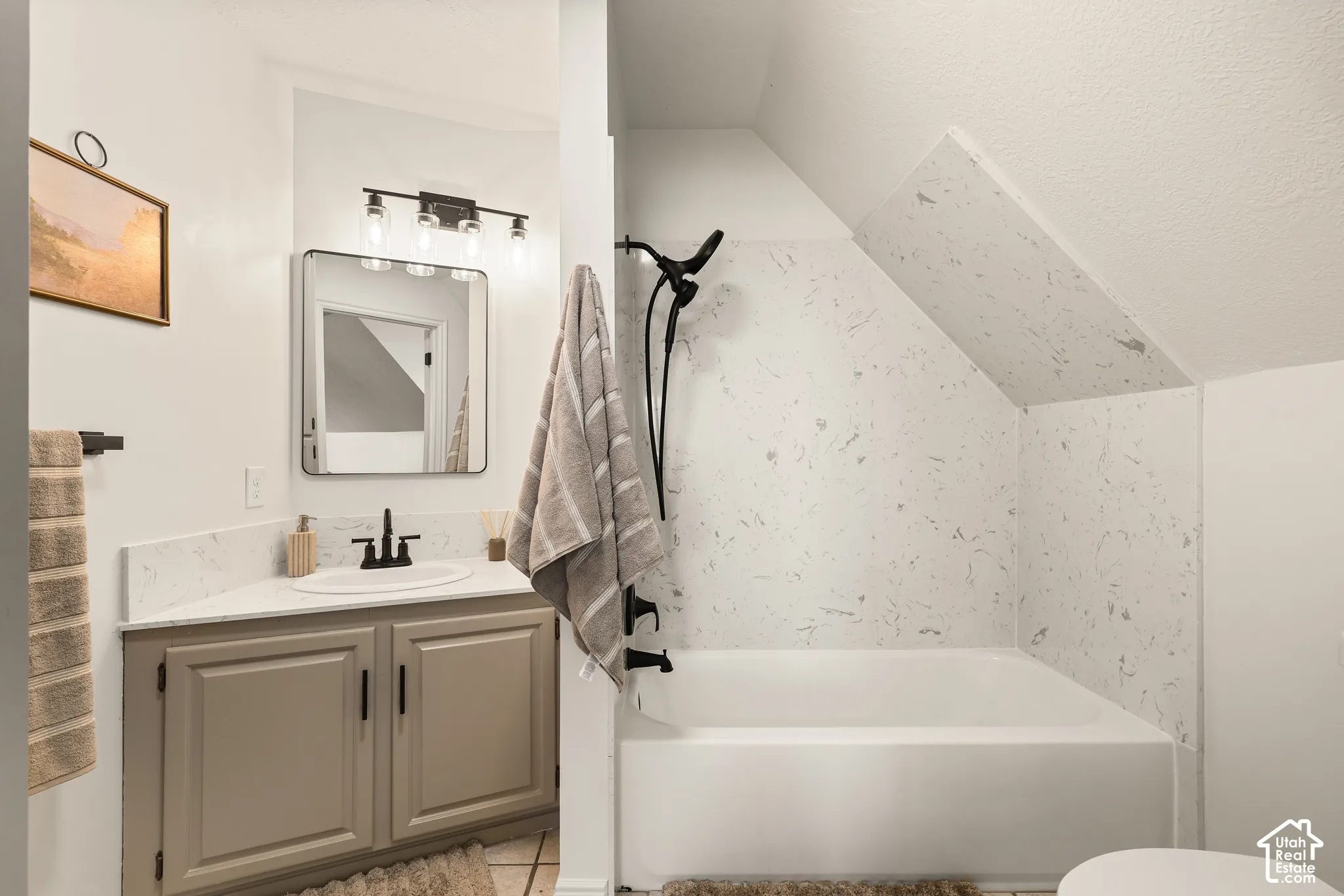 Built-in bathtub with a patterned surround, a single vanity with a solid surface countertop, and a contemporary mirror with integrated lighting