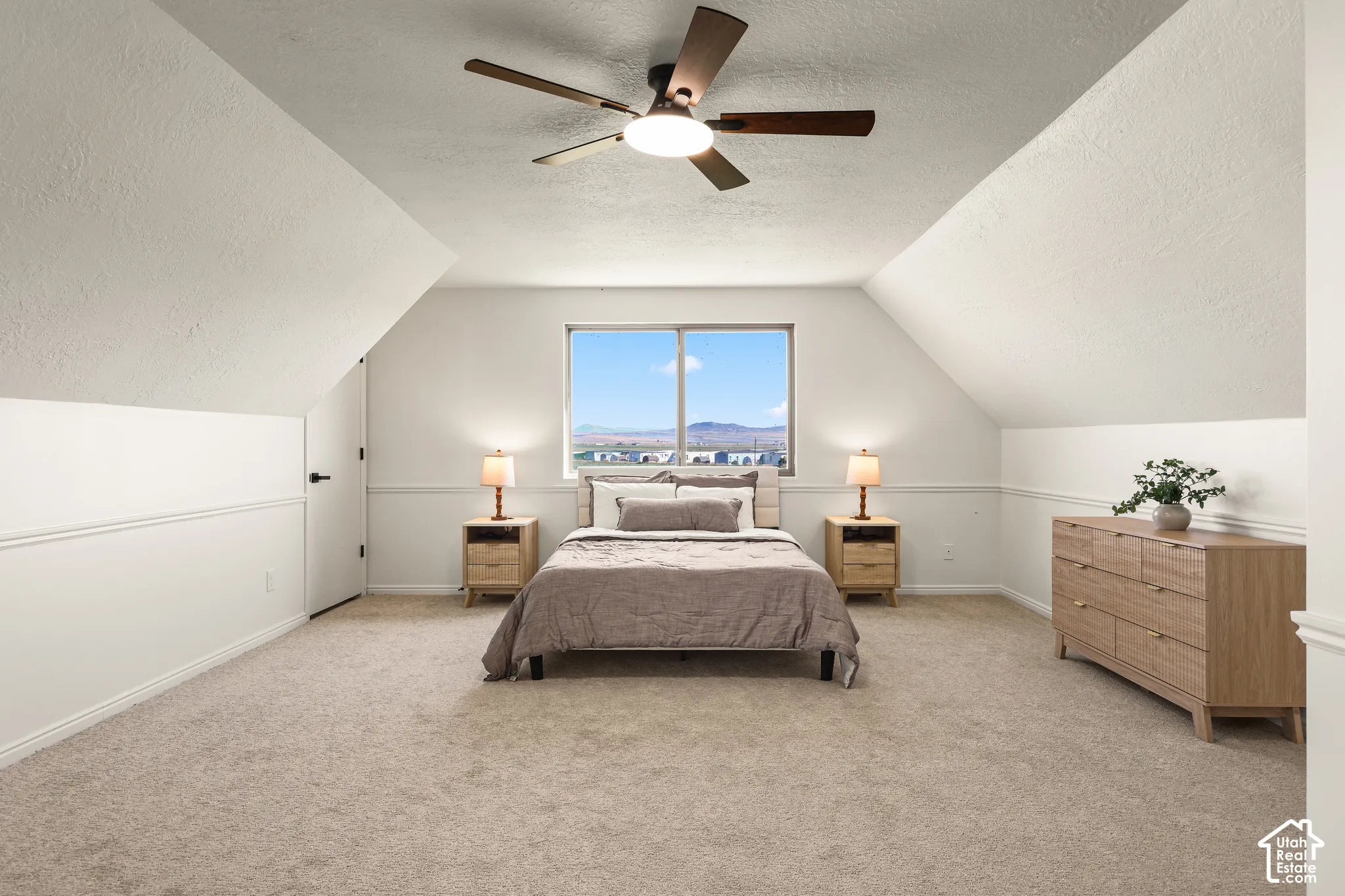 Vaulted ceiling with a ceiling fan, window with distant scenery, wainscoting, and carpeted flooring