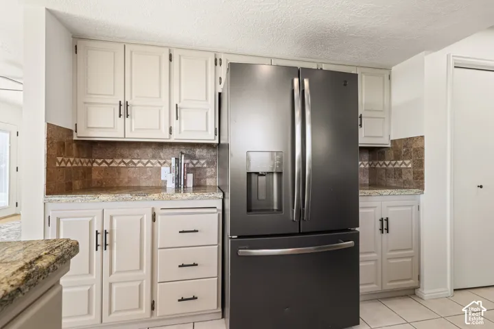 Cream-painted cabinetry with matte black hardware, granite countertops, and a tiled backsplash featuring a decorative accent