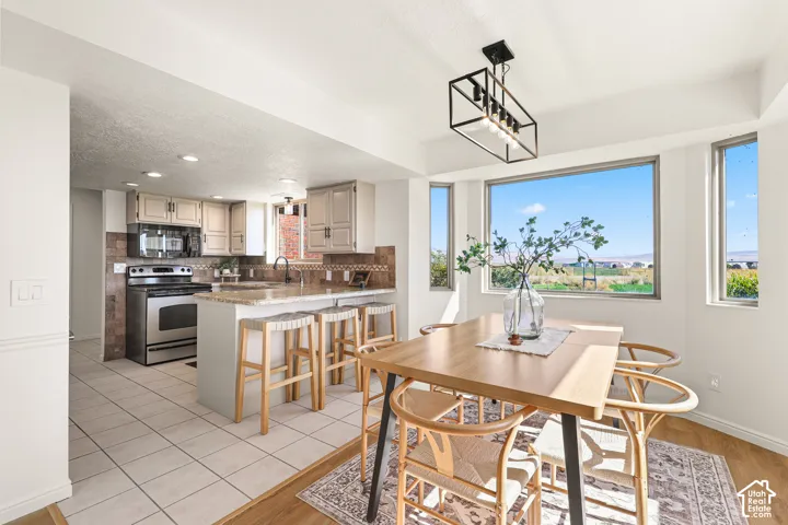 Kitchen and dining area featuring stainless steel appliances, a breakfast bar with granite-style countertop, a tile backsplash, and wood-finish flooring