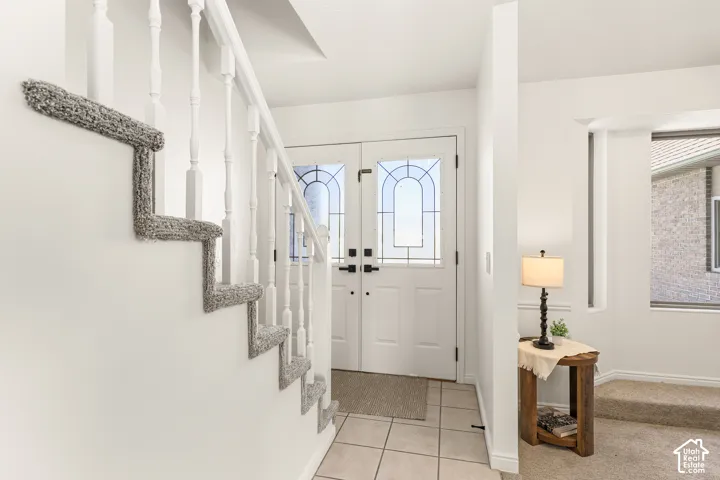 Double entry doors with decorative glass panels, white painted staircase with carpeted treads, and tiled flooring at the entry