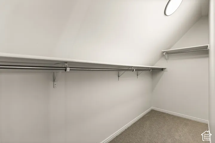 Sloped ceiling closet with two hanging rods and shelving, light-colored carpeting, and a circular overhead light fixture