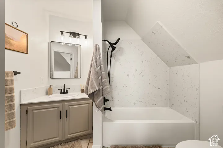 Built-in bathtub with a patterned surround, a single vanity with a solid surface countertop, and a contemporary mirror with integrated lighting