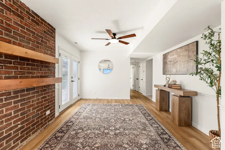 Exposed brick wall with wood mantel shelves, wood-finish flooring, white double doors with glass panels, and a ceiling fan with light