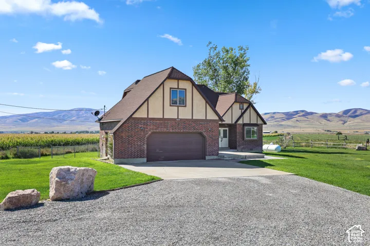 Tudor-style residence featuring a brick and stucco exterior, attached garage, and a gravel driveway