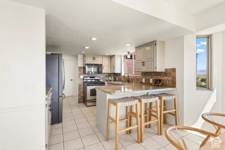 Kitchen featuring light-toned cabinetry, granite countertops, stainless steel appliances, and tile flooring