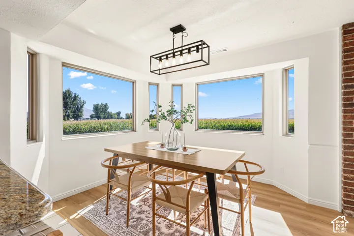 Bay window configuration, wood-finish flooring, exposed brick wall feature, rectangular chandelier, light-toned wall paint