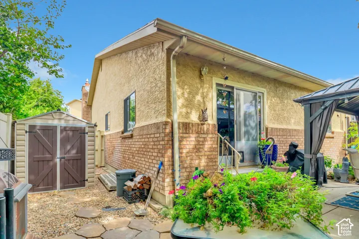 Rear exterior with stucco and brick facade, sliding glass door, and a dedicated storage shed