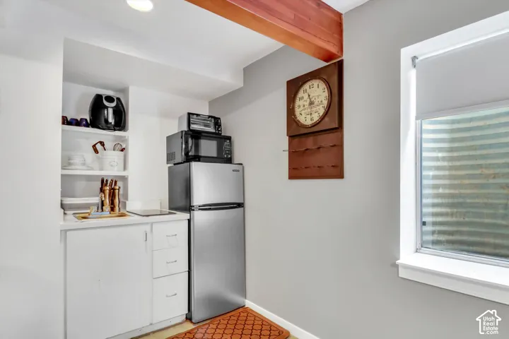 Recessed lighting, wood-beam ceiling, built-in shelving, white cabinetry, and stainless steel compact refrigerator