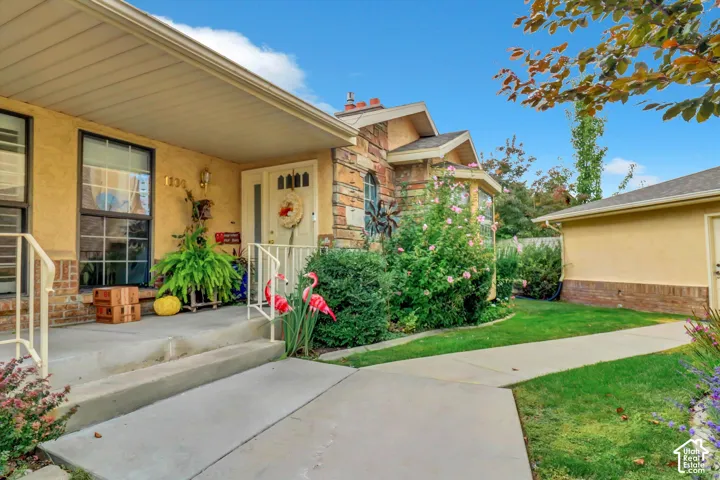 Stucco exterior with stone accents, covered front porch, concrete walkway, established landscaping, and detached garage